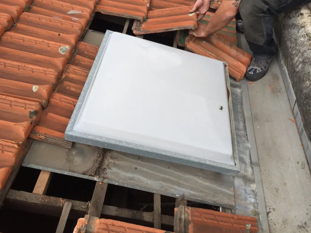 A new skylight fitted into a terracotta tiled roof, with the surrounding tiles lifted and flashing exposed.