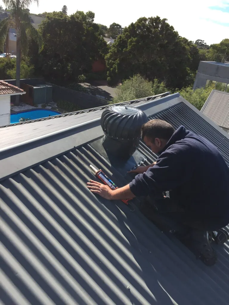 A Mr Roofing tradesman fitting a whirlybird roof vent on a steel roof.